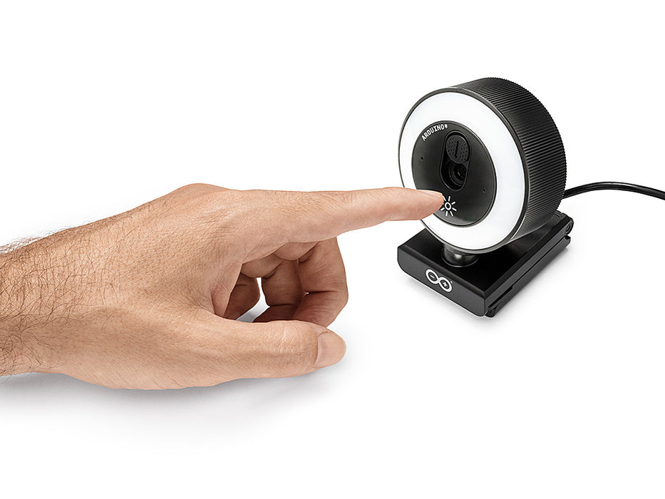 Angled view of a finger tapping the touch brightness control on the Arduino USB Camera, demonstrating the touch-dimmable LED ring light on its clip stand.